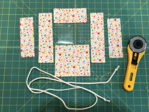 Photo of all the different components (fabric pieces, vinyl, cord) and cutter placed on a cutting mat. 